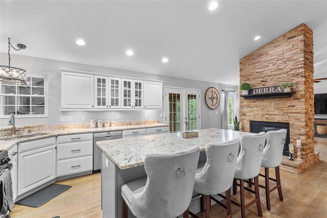 kitchen featuring stainless steel dishwasher, a sink, vaulted ceiling, white cabinets, and a center island