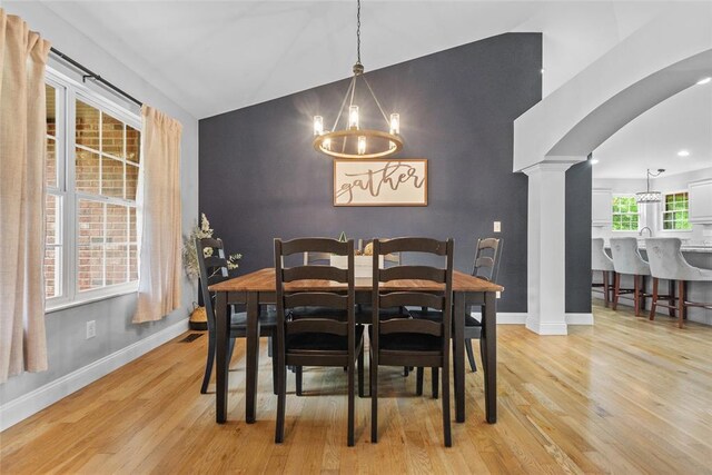 dining space featuring a chandelier, ornate columns, vaulted ceiling, light wood finished floors, and recessed lighting