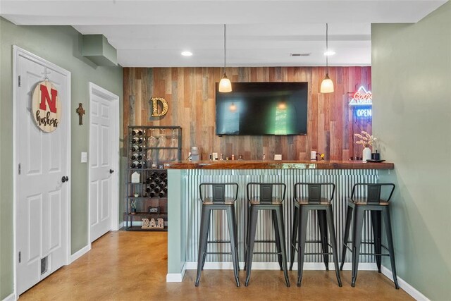 indoor bar featuring wood walls, baseboards, recessed lighting, concrete flooring, and decorative light fixtures