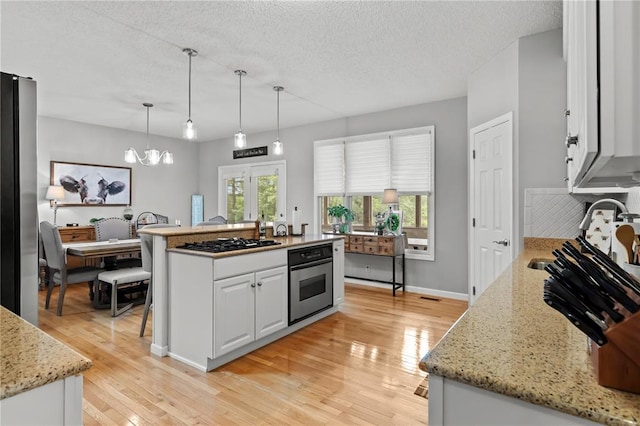 2056 Hawks Landing Dr, Lake St Louis, MO 63367 - kitchen with stainless steel oven, black gas stovetop, white cabinets, light wood-style floors, and a textured ceiling
