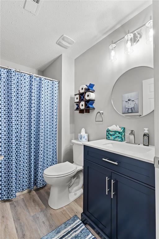 2056 Hawks Landing Dr, Lake St Louis, MO 63367 - bathroom featuring wood finished floors, a textured ceiling, toilet, vanity, and curtained shower