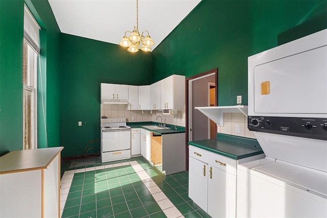 3534 Washington Ave, Saint Louis, MO 63103 - kitchen with white range with electric cooktop, stacked washer and clothes dryer, high vaulted ceiling, white cabinetry, and a chandelier