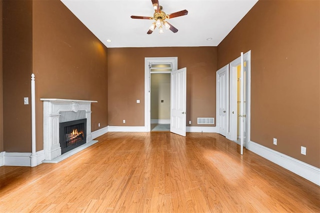 3534 Washington Ave, Saint Louis, MO 63103 - unfurnished living room with a ceiling fan, light wood-style flooring, a warm lit fireplace, and baseboards