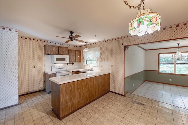 kitchen featuring white appliances, a sink, wallpapered walls, light countertops, and a peninsula
