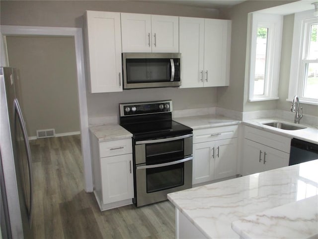 kitchen with appliances with stainless steel finishes, light wood finished floors, light stone countertops, white cabinetry, and a sink