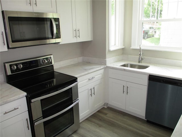 kitchen with stainless steel appliances, a sink, white cabinetry, and light stone countertops