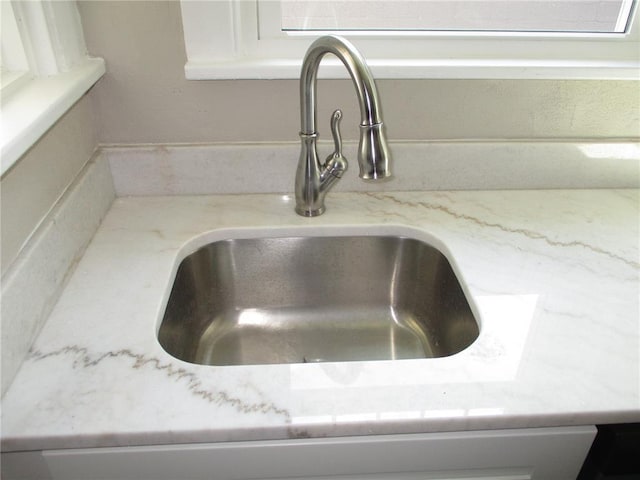 kitchen view of a sink, light stone countertops, and white cabinets