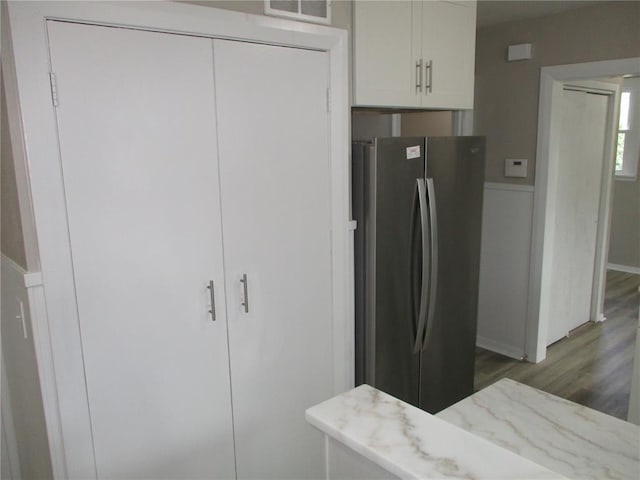 kitchen with freestanding refrigerator, wood finished floors, light stone countertops, and white cabinetry