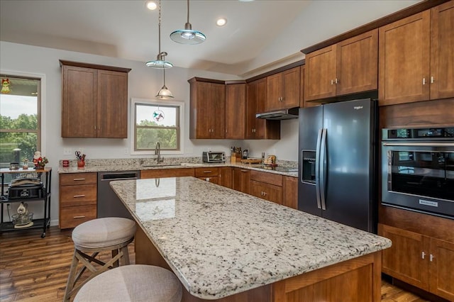 kitchen with black appliances, a sink, dark wood-type flooring, light stone countertops, and decorative light fixtures