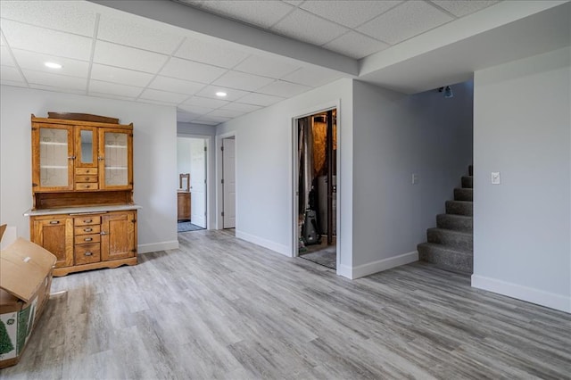 unfurnished living room with a drop ceiling, baseboards, stairs, light wood finished floors, and recessed lighting