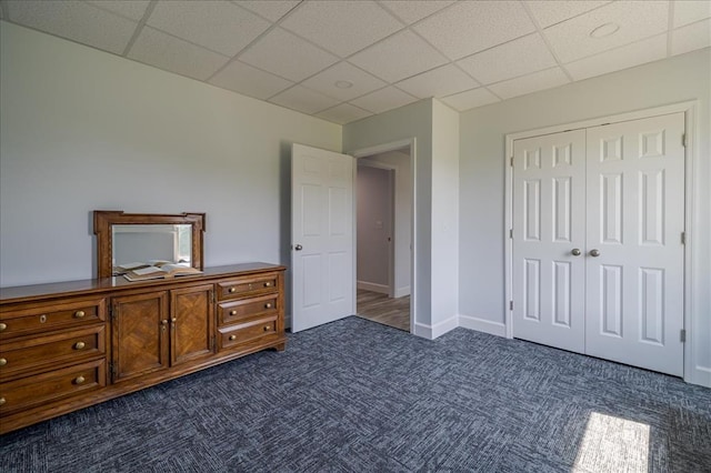 unfurnished bedroom with dark colored carpet, a drop ceiling, a closet, and baseboards