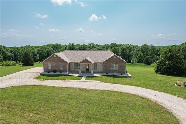 single story home with a front yard, a forest view, covered porch, and curved driveway