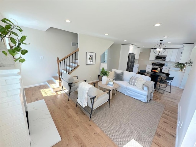 living room featuring stairway, light wood finished floors, recessed lighting, baseboards, and a chandelier