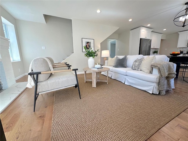 living area with light wood finished floors, a chandelier, recessed lighting, baseboards, and stairs