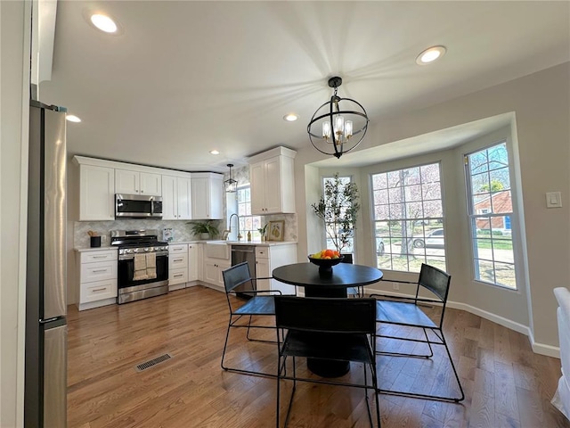 dining space featuring a chandelier, baseboards, recessed lighting, and light wood finished floors