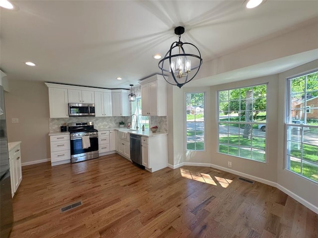 kitchen with stainless steel appliances, a sink, decorative backsplash, a chandelier, and light countertops