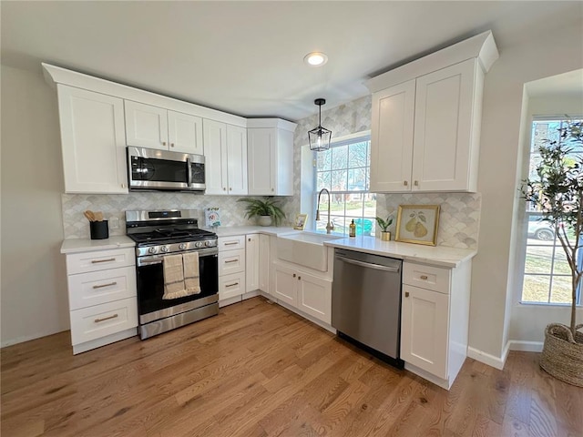 kitchen featuring appliances with stainless steel finishes, a sink, light countertops, white cabinetry, and recessed lighting