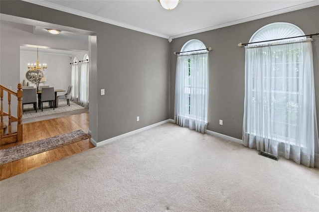 empty room featuring a chandelier, carpet flooring, ornamental molding, and baseboards
