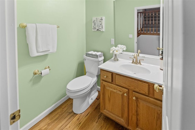 half bath featuring wood finished floors, toilet, baseboards, and vanity
