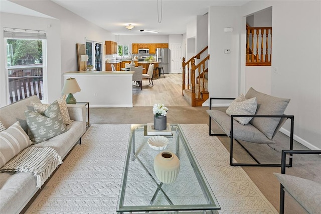 living area featuring stairway, light colored carpet, and baseboards