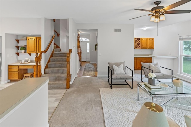 living room with ceiling fan, stairway, baseboards, and light carpet