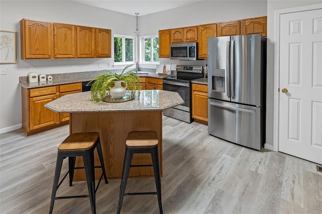 kitchen featuring appliances with stainless steel finishes, brown cabinetry, light wood finished floors, and light stone counters