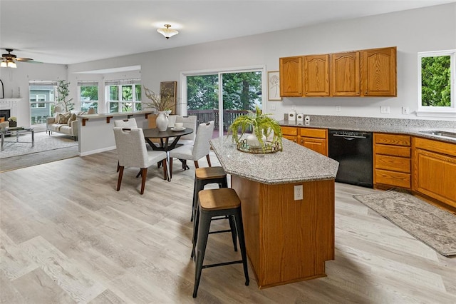 kitchen with black dishwasher, open floor plan, light wood-style floors, a breakfast bar area, and brown cabinets