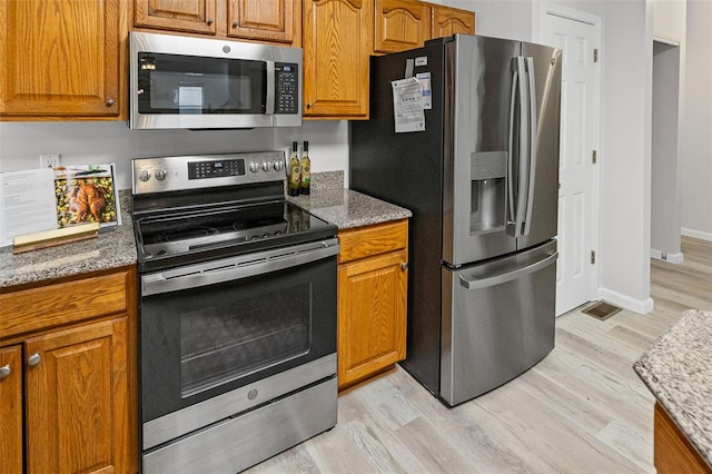 kitchen with appliances with stainless steel finishes, light wood-style flooring, brown cabinetry, and light stone counters