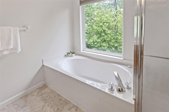 bathroom featuring a bath, baseboards, and marble look tile flooring