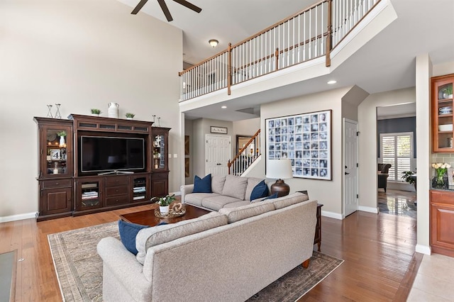 living room featuring ceiling fan, baseboards, a high ceiling, stairway, and wood finished floors
