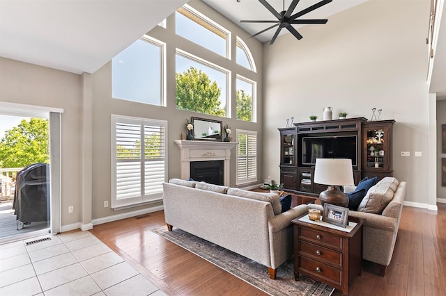 living room featuring a towering ceiling, a fireplace, healthy amount of natural light, baseboards, and ceiling fan