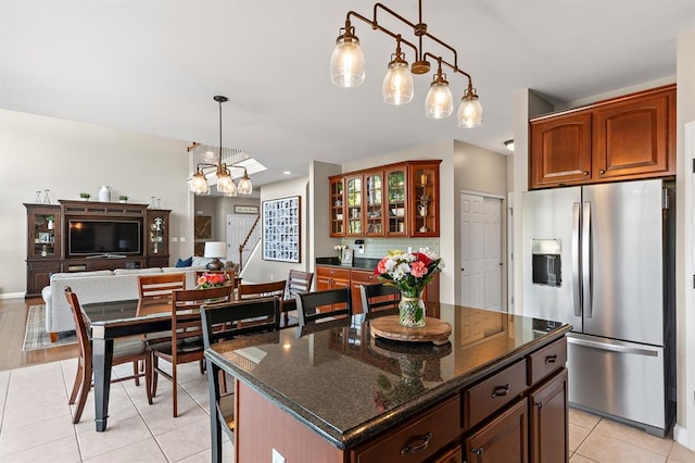kitchen featuring stainless steel refrigerator with ice dispenser, light tile patterned floors, glass insert cabinets, tasteful backsplash, and pendant lighting