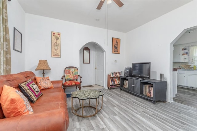 living area with arched walkways, a ceiling fan, wood finished floors, and baseboards