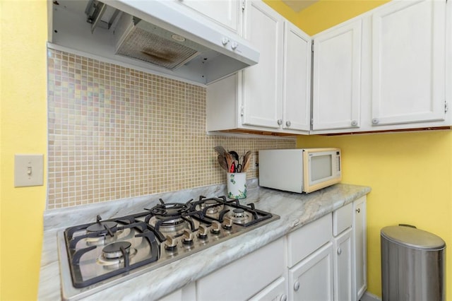 kitchen featuring white microwave, stainless steel gas stovetop, light countertops, white cabinets, and backsplash