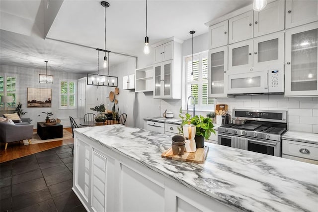 kitchen with gas range, white microwave, white cabinetry, a chandelier, and backsplash