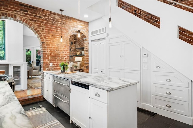 kitchen featuring brick wall, white cabinets, arched walkways, light stone countertops, and decorative light fixtures