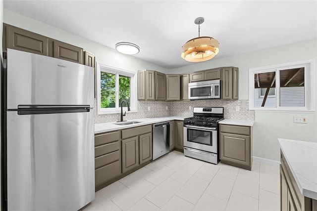 kitchen featuring stainless steel appliances, a sink, light countertops, decorative backsplash, and decorative light fixtures