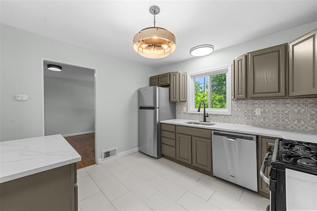 kitchen featuring appliances with stainless steel finishes, a sink, backsplash, decorative light fixtures, and light stone countertops