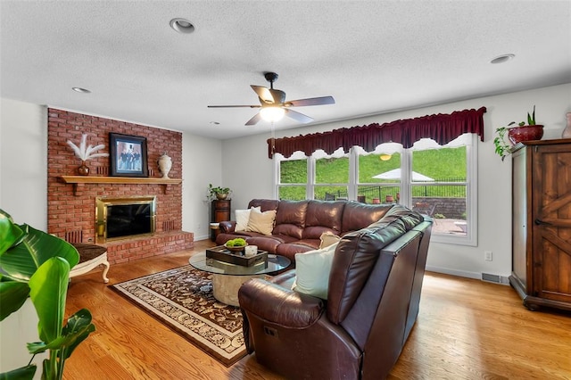 1711 El Rio Dr, Cape Girardeau, MO 63701 - living area featuring a textured ceiling, light wood finished floors, ceiling fan, baseboards, and a brick fireplace