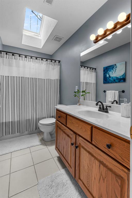 1711 El Rio Dr, Cape Girardeau, MO 63701 - bathroom with a skylight, lofted ceiling, tile patterned flooring, vanity, and toilet