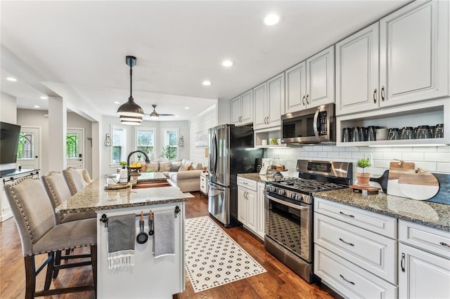 kitchen with stainless steel appliances, open floor plan, light stone countertops, tasteful backsplash, and recessed lighting