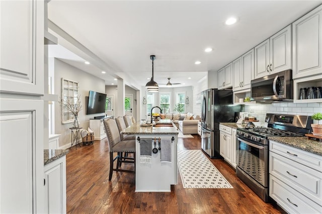 kitchen with stainless steel appliances, open floor plan, dark stone counters, and recessed lighting