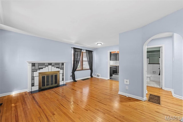 8261 Watson Rd, Saint Louis, MO 63119 - unfurnished living room featuring a fireplace, light wood-style flooring, and arched walkways