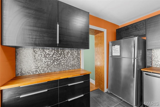 8261 Watson Rd, Saint Louis, MO 63119 - kitchen with stainless steel appliances, butcher block countertops, dark cabinetry, tasteful backsplash, and dark tile patterned flooring