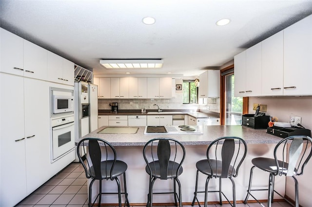 kitchen with white appliances, a peninsula, tasteful backsplash, a breakfast bar, and white cabinetry