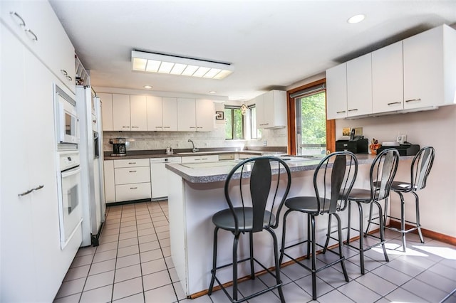 kitchen featuring a peninsula, white appliances, decorative backsplash, light tile patterned floors, and recessed lighting