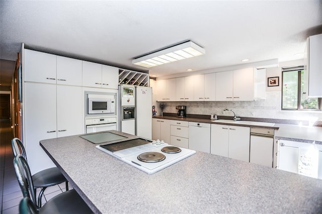 kitchen with white appliances, a kitchen bar, white cabinets, and decorative backsplash