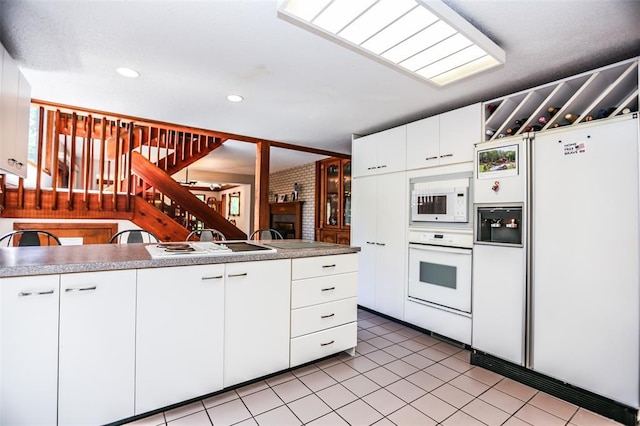 kitchen featuring white appliances, light tile patterned flooring, white cabinetry, recessed lighting, and a brick fireplace