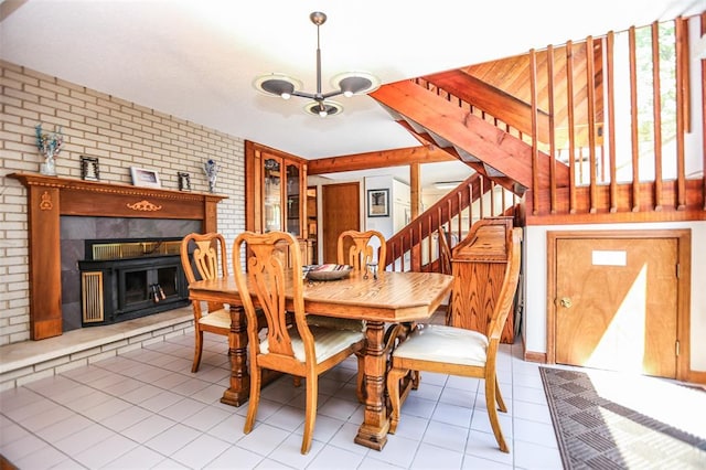 dining area featuring brick wall, stairway, a chandelier, a fireplace, and tile patterned flooring