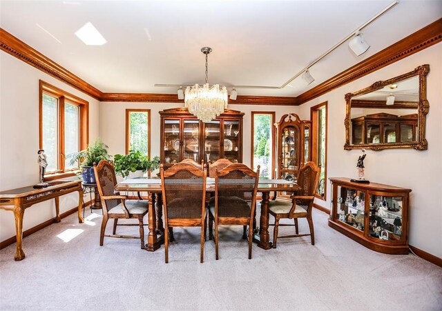 dining space featuring a chandelier, ornamental molding, light colored carpet, baseboards, and rail lighting